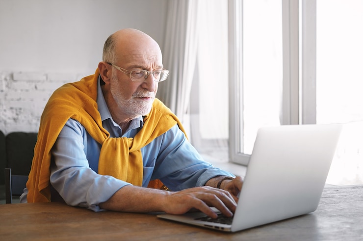 Foto grátis conceito de pessoas, estilo de vida, idade, negócios, emprego, carreira e ocupação. foto interna de um trabalhador de escritório sério focado de óculos, camisa azul e suéter digitando em um laptop genérico, digitando rápido