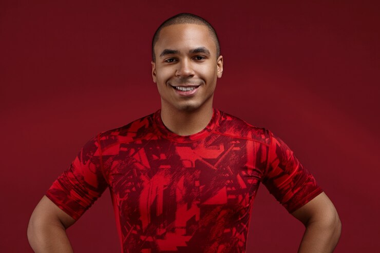 Foto grátis conceito de pessoas, estilo, esportes e moda. foto recortada de um jovem afro-americano de 20 anos, bem definido e positivo, posando no estúdio usando uma camiseta vermelha da moda, olhando e sorrindo para a câmera