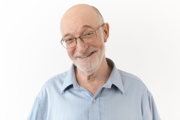 Conceito de pessoas, idade, positividade, alegria e felicidade. Homem idoso fofo e bonito vestindo camisa azul e óculos retangulares, sorrindo amplamente, rindo de sua própria piada, expressando emoções positivas