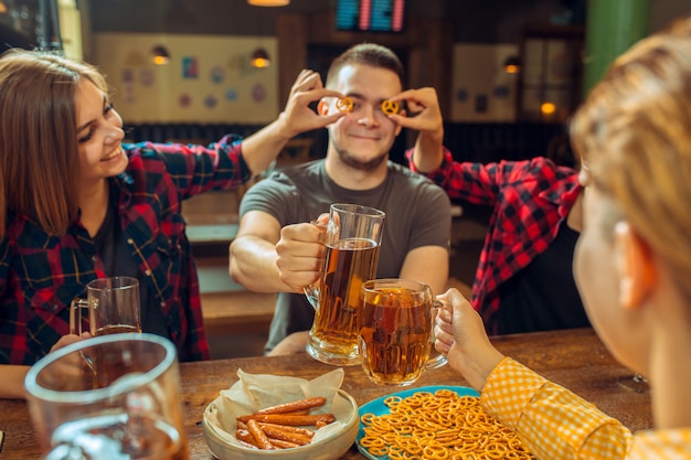 Conceito de pessoas, lazer, amizade e comunicação - amigos felizes bebendo cerveja, conversando e tilintar de copos no bar ou pub