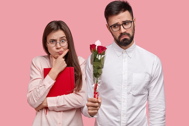 Conceito de pessoas, namoro e relacionamento. Homem barbudo descontente com uma camisa branca elegante dá rosas para namorada e quer se desculpar