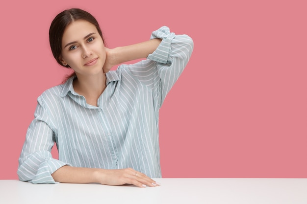 Conceito de pessoas, trabalho, carreira e ocupação. Empregado atraente jovem europeu positivo com camisa listrada, trabalhando no escritório. Aluna muito fofa sentada na mesa branca, esticando os braços