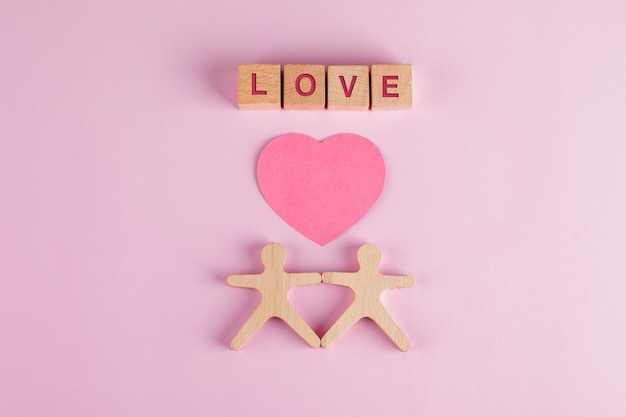 Conceito de relacionamento com papel cortado coração, cubos de madeira, modelos humanos na mesa rosa plana leigos.