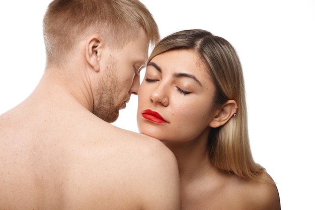 Conceito de romance e paixão. Imagem de um atraente casal adulto caucasiano acariciando: mulher bonita com batom vermelho e argola no nariz fechando os olhos, inalando o cheiro bom do corpo de seu homem barbudo