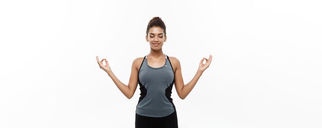 Conceito de saúde e fitness Linda senhora africana americana em roupas de fitness fazendo ioga e meditação Isolado em fundo branco