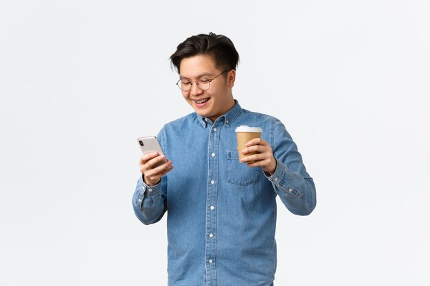 Conceito de tecnologia e lazer de estilo de vida sorrindo estudante universitário homem asiático, tendo pausa para beber tak ...