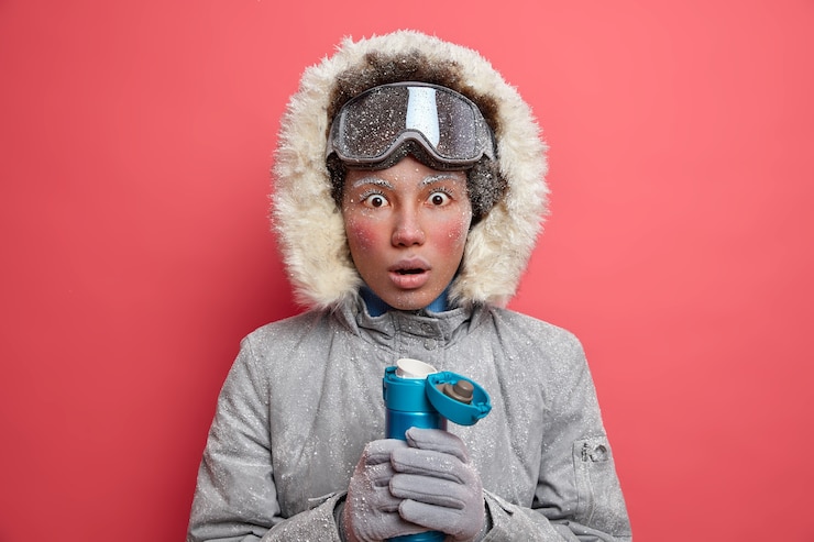 Foto grátis conceito de tempo de inverno. surpresa jovem étnica com rosto vermelho usa jaqueta quente e capuz passa o tempo livre no hobby favorito esquiar ou praticar snowboard.