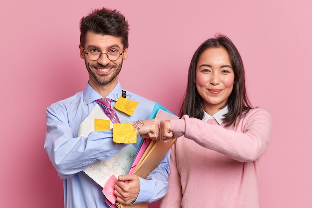 Foto grátis conceito de trabalho em equipe. felizes colegas profissionais diversos fazem fist bump trabalhar juntos no homem comum de trabalho de projeto coberto com papéis e notas adesivas, feliz por alcançar o sucesso e terminar a tarefa.