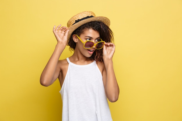 Conceito de viagem - close up retrato jovem e bela atrativa mulher afro-americana com chapéu de moda sorridente e alegre expressão. fundo amarelo do estúdio pastel. copie o espaço.