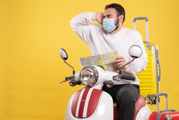 Conceito de viagem com cara emocional em máscara médica sentado em uma motocicleta com uma mala amarela nela