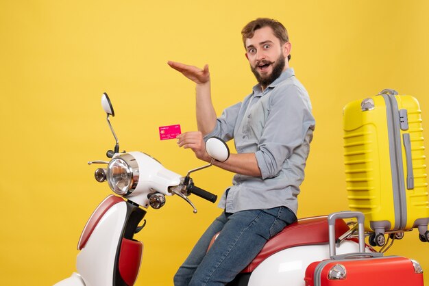 Conceito de viagens com jovem homem barbudo confiante e emocional sentado na motocicleta segurando o cartão do banco em amarelo