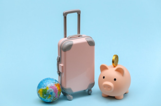 Conceito de viagens internacionais. mini mala de viagem de plástico rosa com globo, cofrinho sobre fundo azul. estilo minimalista