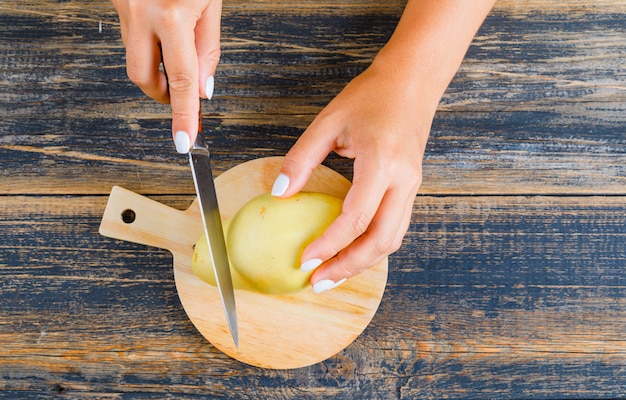 Conceito do alimento na configuração de madeira e de plano de fundo da placa de corte. mulher cortando pêra usando faca.
