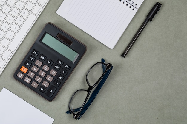 Conceito financeiro com caderno, papel, caneta, calculadora, teclado, óculos no fundo cinza plana leigos.