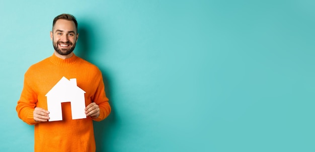 Conceito imobiliário jovem feliz procurando por aluguel de casa segurando papel de casa e sorrindo st