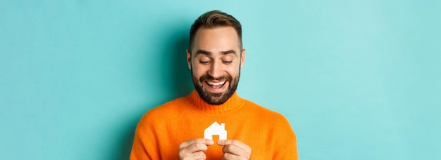 Conceito imobiliário jovem feliz procurando por aluguel de casa segurando papel de casa e sorrindo st