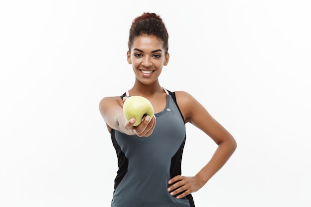 Conceito saudável e de fitness - linda dama africana americana em roupas de fitness cinza segurando maçã verde. isolado no fundo branco.