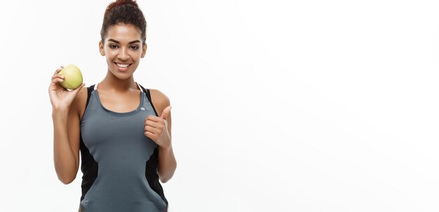 Conceito saudável e fitness Linda dama africana americana em roupas cinzas de fitness segurando maçã verde isolada em fundo branco