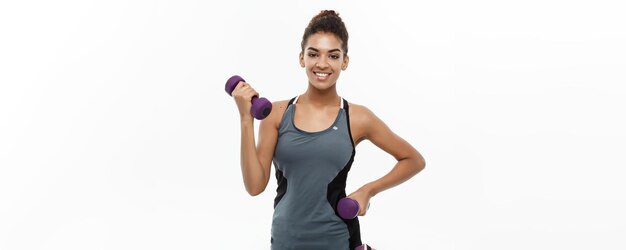 Conceito saudável e fitness Linda dama africana americana em treino de roupas fitness com haltere isolado em fundo branco