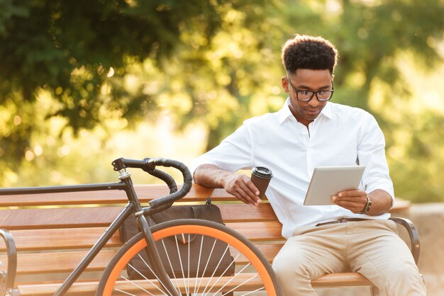 Concentrado jovem Africano usando tablet bebendo café.