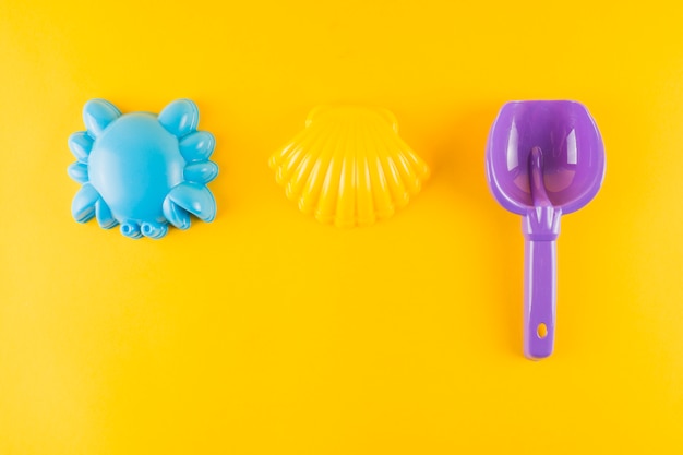 Concha de vieira de plástico azul; caranguejo e pá de plástico em fundo amarelo