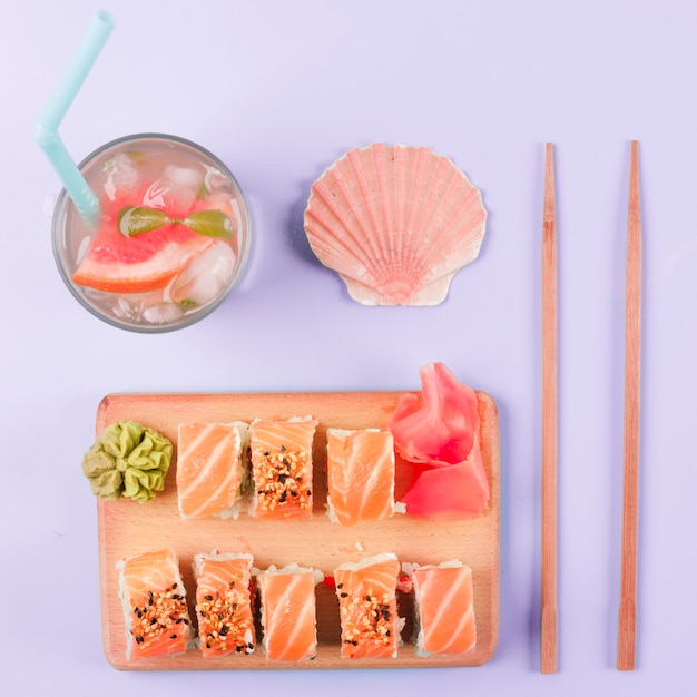 Foto grátis concha de vieira; suco de toranja; pauzinhos; sushi de salmão servido com wasabi e gengibre em conserva em cortar placa contra o pano de fundo roxo