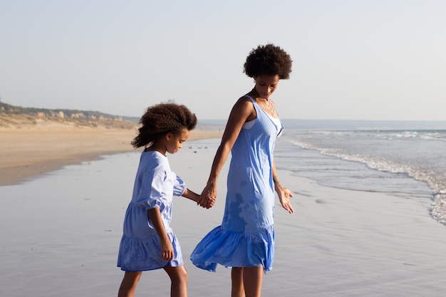Foto grátis concurso mãe e filha de férias. família afro-americana em lindos vestidos andando na praia, se divertindo, de mãos dadas. família, viajando, conceito de paternidade