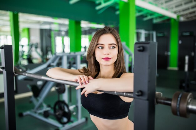 Concurso mulher com longos cabelos morenos e olhos grandes, posando no moderno centro de fitness perto do espelho em roupas esportivas curtas