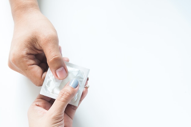 Condom na mão masculina e na mão feminina, dê um conceito de sexo seguro ao preservativo no fundo branco