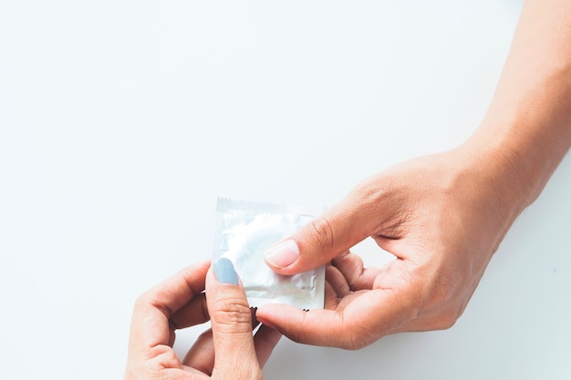 Condom na mão masculina e na mão feminina, dê um conceito de sexo seguro ao preservativo no fundo branco