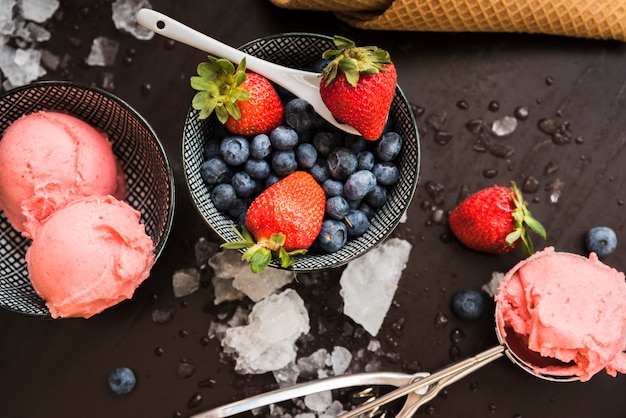 Cone de waffle perto de frutas frescas e sorvete em pratos e colher entre gelo derretido