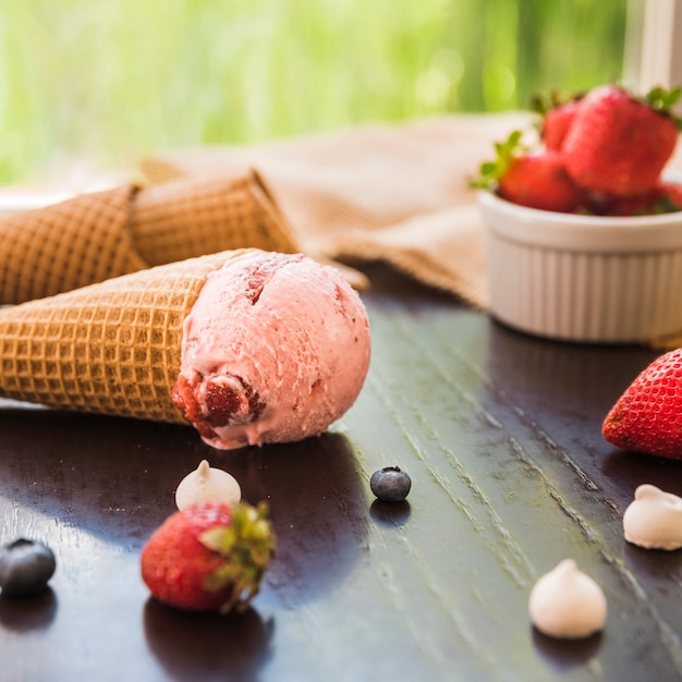 Cones de waffle com sorvete perto de frutas frescas na tigela e guardanapo na mesa