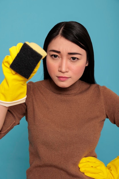 Foto grátis confiança jovem trabalhadora doméstica asiática séria de tarefas usando luvas amarelas segurando uma esponja, conceito de limpeza em casa, dona de casa fiel cansada e sobrecarregada de tarefas do dia a dia