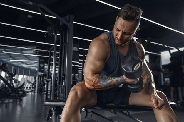 Confiante. Jovem atleta caucasiana musculosa praticando na academia com os pesos. Modelo masculino fazendo exercícios de força, treinando a parte superior do corpo. Bem-estar, estilo de vida saudável, conceito de musculação.