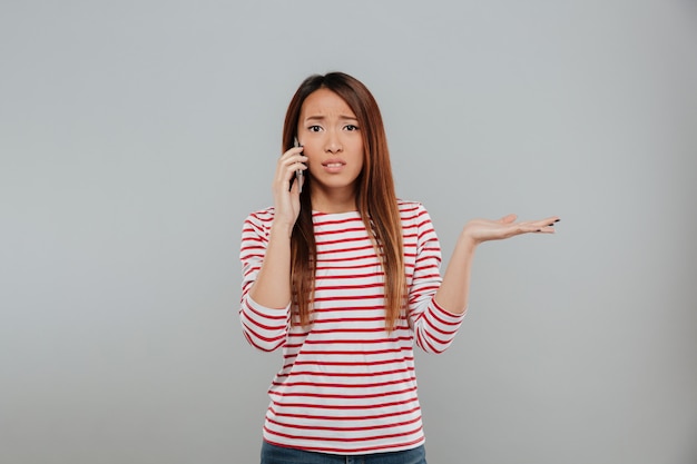 Confusa jovem mulher asiática falando por telefone