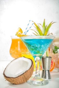 Conjunto de bebidas coloridas de verão. vários coquetéis e bebidas alcoólicas brilhantes, em copos diferentes, com frutas tropicais no espaço de cópia de fundo branco