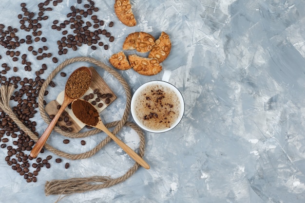 Conjunto de biscoitos, grãos de café, café moído, corda e café em uma xícara em gesso cinza e fundo de pedaço de madeira. vista do topo.