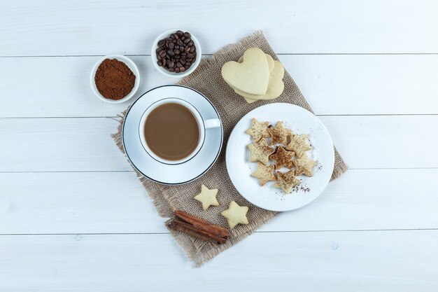 Conjunto de biscoitos, paus de canela, grãos de café, café moído e café em uma xícara de madeira e pedaço de fundo de saco. vista do topo.