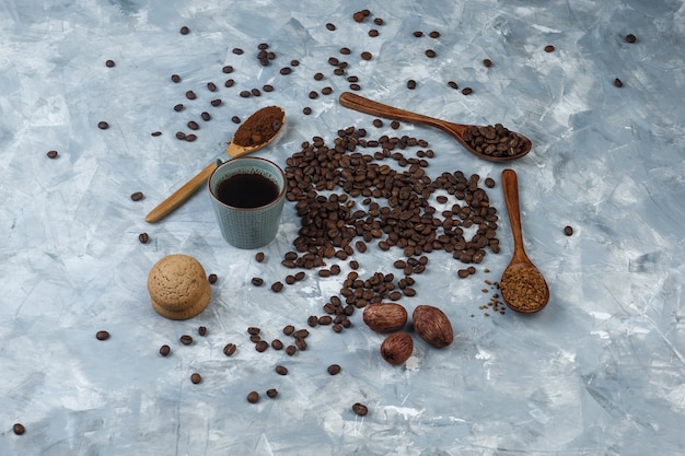 Conjunto de café instantâneo, farinha de café, grãos de café em colheres de madeira, biscoitos e grãos de café, xícara de café sobre um fundo de mármore azul claro. vista de alto ângulo.