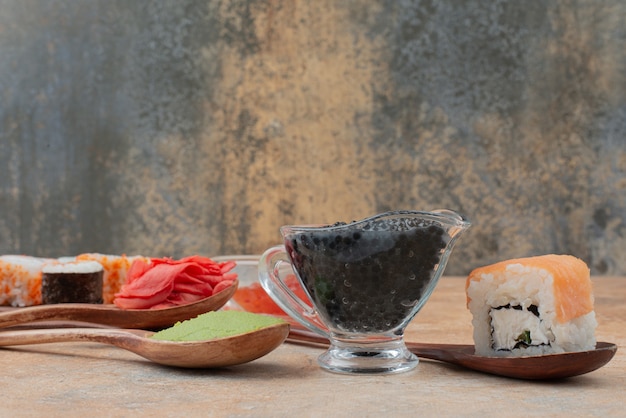 Conjunto de delicioso sushi roll com colher e molho de soja na superfície de mármore