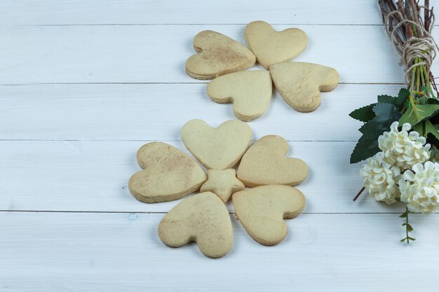 Conjunto de flores e biscoitos em forma de coração em um fundo branco de placa de madeira. fechar-se.