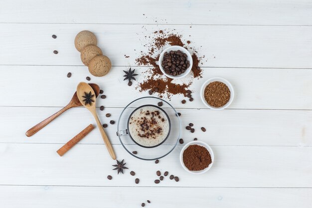 Conjunto de grãos de café, café moído, especiarias, biscoitos, colheres de madeira e café em uma xícara com fundo de madeira. vista do topo.