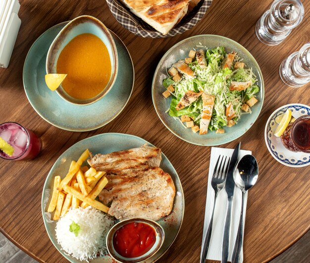 Conjunto de jantar com salada caesar, sopa de lentilha e filé de frango servido com arroz e batata frita