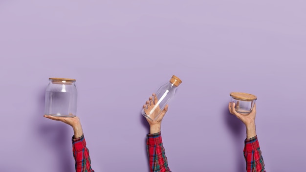 Conjunto de mãos masculinas segurando uma jarra de vidro vazia, garrafa e recipiente com tampa orgânica