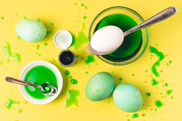 Conjunto de ovos de Páscoa verde entre borrões, colher e líquido de tintura