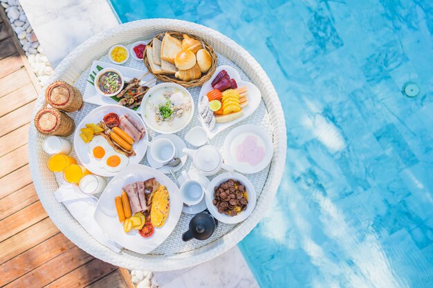 Conjunto de pequeno-almoço flutuante na bandeja com omelete de ovo frito salsicha pão de presunto fruta leite suco de café