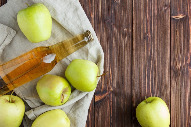 Conjunto de suco de maçã e maçãs verdes em um pano e fundo de madeira. configuração plana. espaço para texto