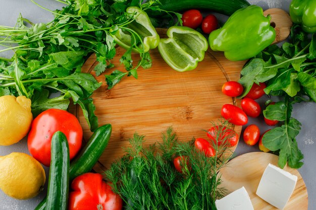 Conjunto de tomate, sal, queijo, pimenta verde, limão e verduras em uma tábua sobre uma superfície cinza