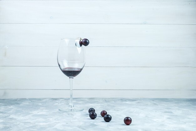Conjunto de um copo de vinho e uvas pretas sobre fundo cinza e de madeira sujo. vista lateral.