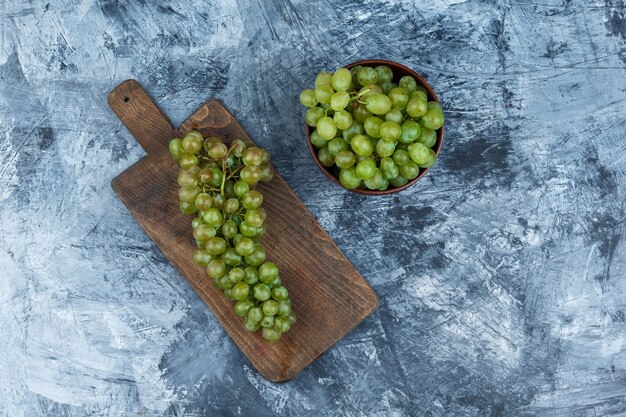 Conjunto de uvas brancas na tábua e uvas brancas em uma tigela sobre um fundo de mármore azul escuro. colocação plana.